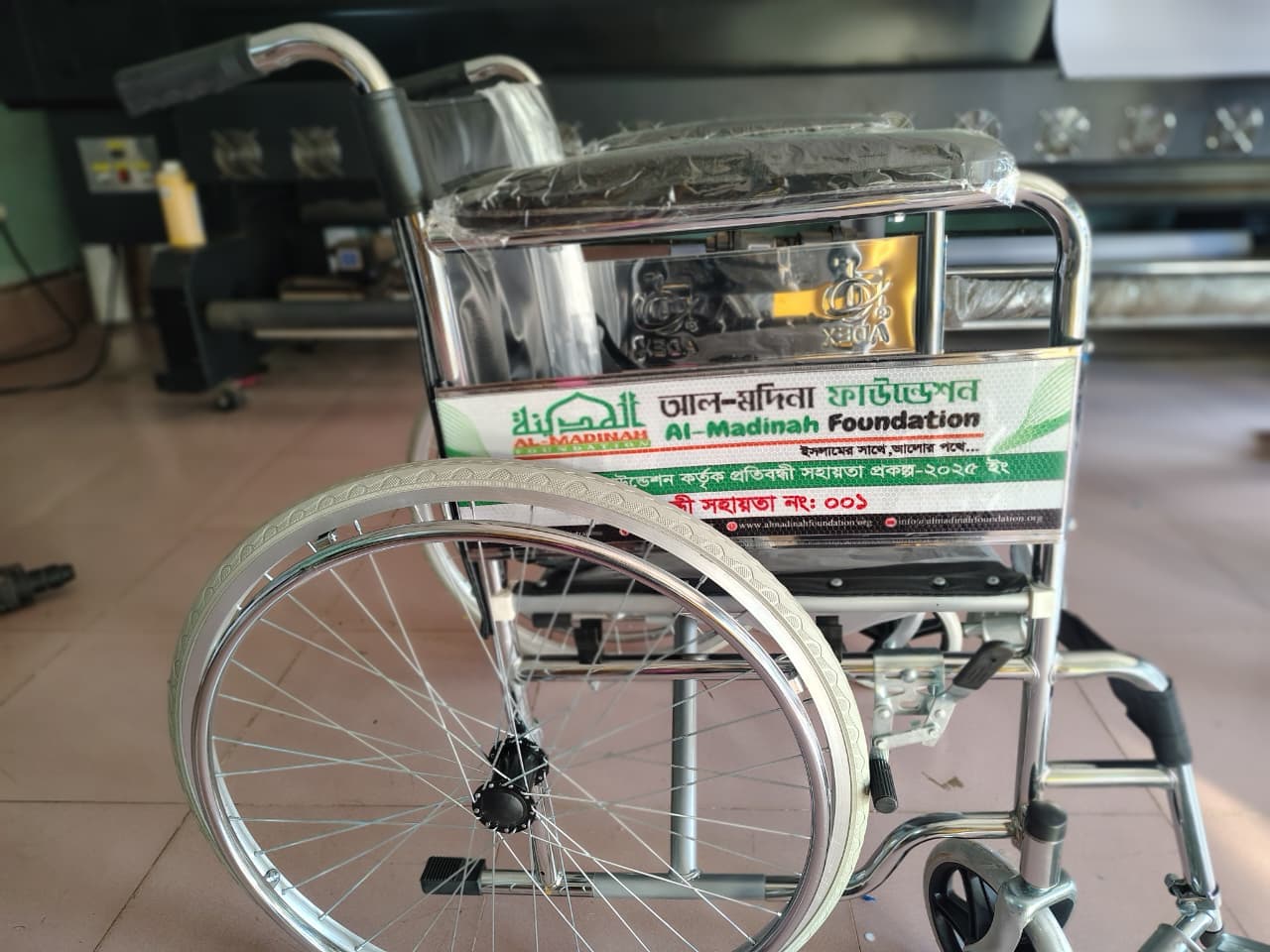 একটি নতুন হুইলচেয়ারের পেছনে সহায়তা প্রকল্পের পরিচিতি লাগানো আছে।