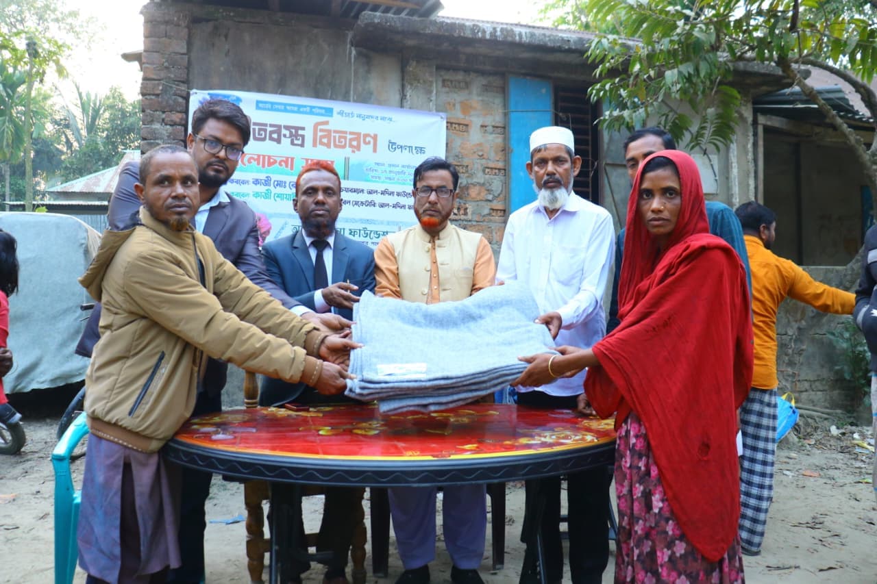লাল ওড়না পরা একজন নারী খোলা উঠোনে ধূসর কম্বল গ্রহণ করছেন।