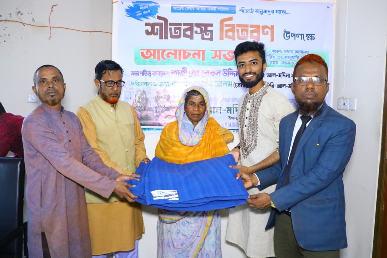 হলুদ ওড়না পরা একজন নারীর হাতে কয়েকজন নীল কম্বল তুলে দিচ্ছেন।