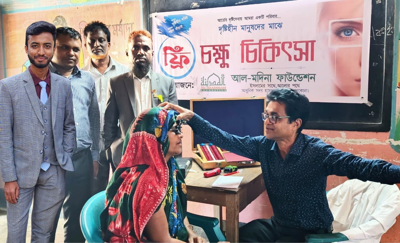 চক্ষুসেবার ব্যানারের সামনে একজনের চোখ পরীক্ষা করা হচ্ছে; পাশে কয়েকজন দাঁড়িয়ে।