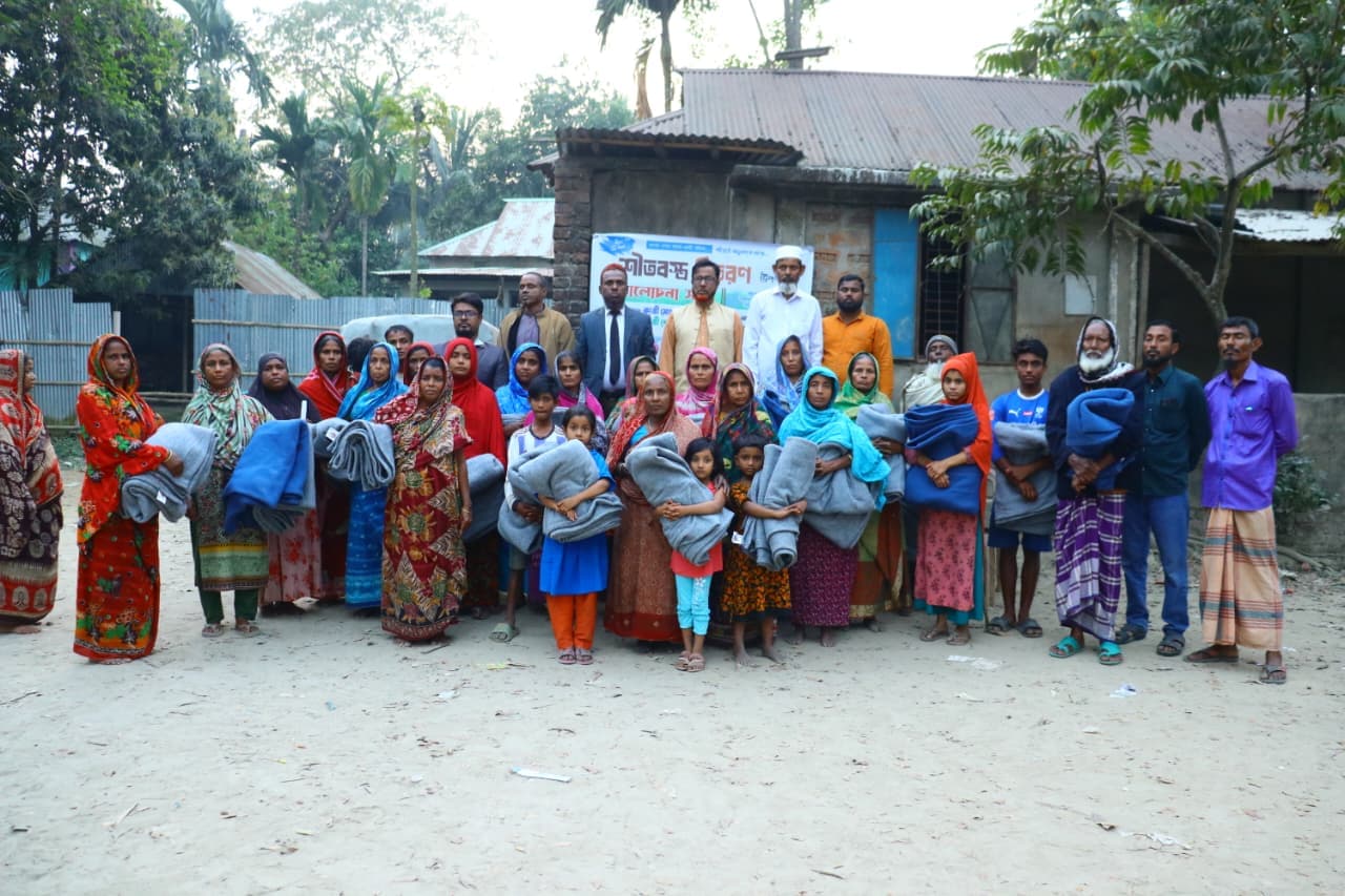 খোলা উঠোনে নারী, পুরুষ ও শিশুরা কম্বল হাতে একসঙ্গে দাঁড়িয়ে আছেন।