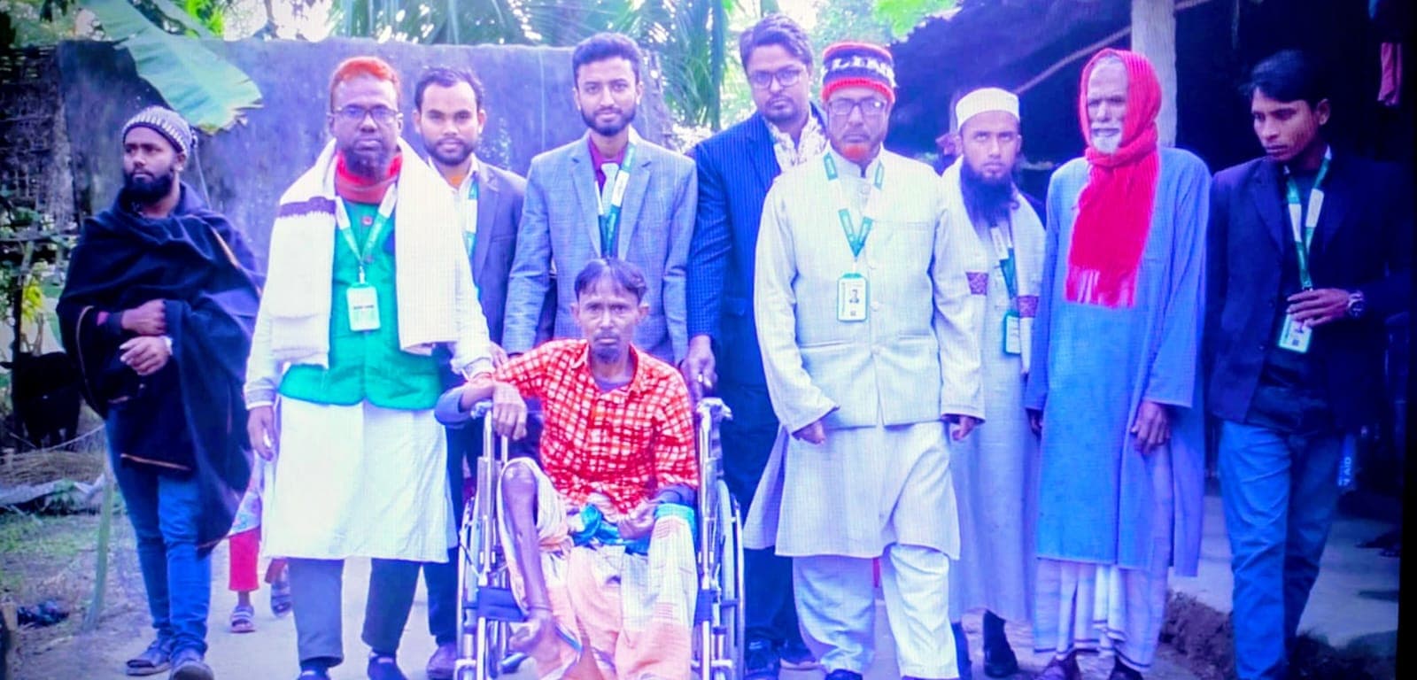 একজন হুইলচেয়ার ব্যবহারকারীকে ঘিরে খোলা জায়গায় কয়েকজন দাঁড়িয়ে আছেন।